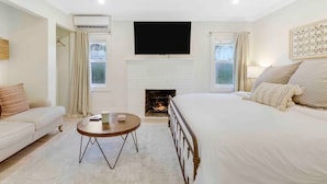 Un dormitorio con cama, televisor montado en la pared, chimenea y ventana.