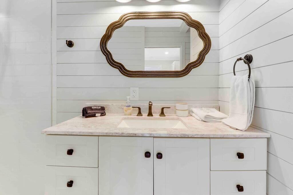 Un baño con encimera de mármol, un lavabo con grifo dorado, un espejo con marco dorado y un perchero para toallas.