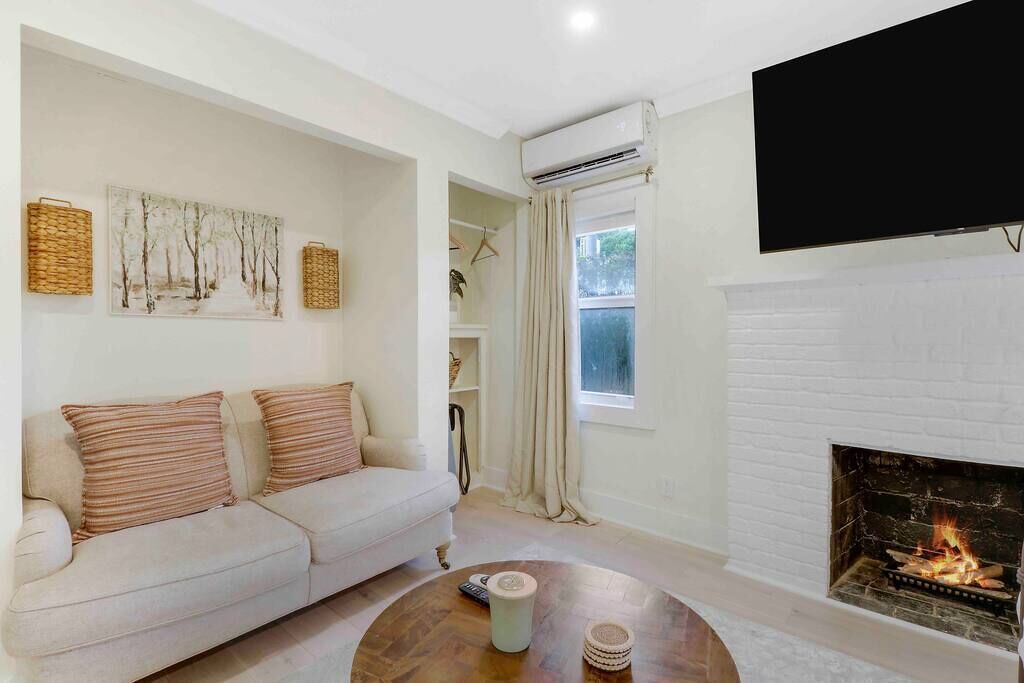 A living room with a white sofa, a fireplace, a flat-screen TV, and artwork on the wall.