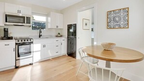Una cocina moderna con armarios blancos, electrodomésticos de acero inoxidable y una mesa de comedor de madera.