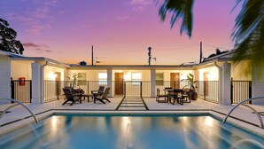 Zona junto a la piscina con piscina, sillas de descanso y un área de estar cubierta.