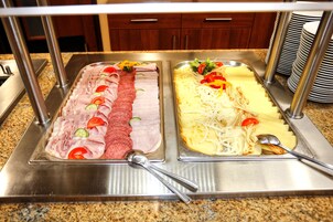 Montaje de bufé con dos bandejas de comida: una con carnes y vegetales en rodajas, y otra con pasta y queso.