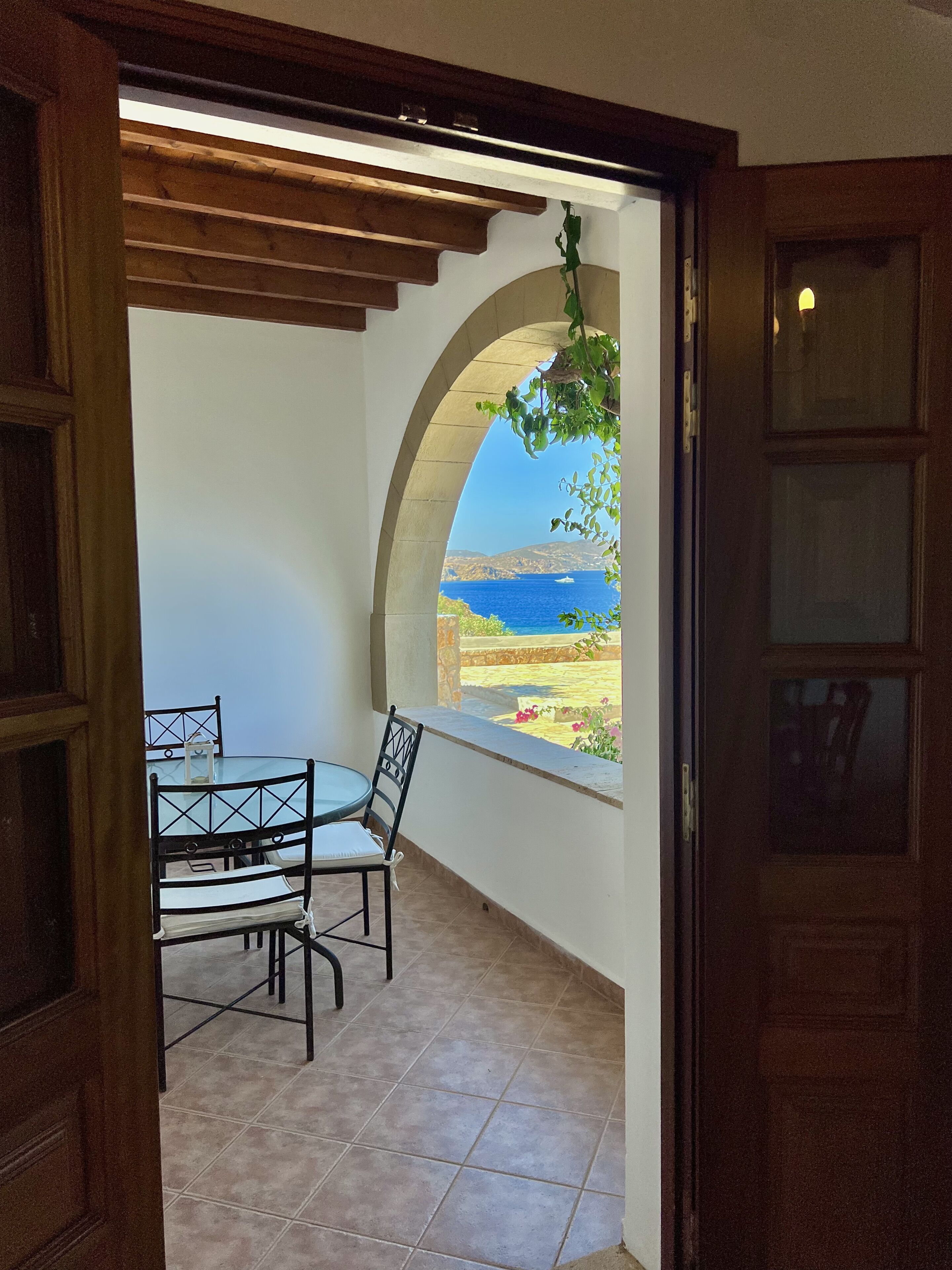 Un balcón con mesa y sillas, y una ventana en arco con vistas al paisaje costero.