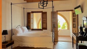 A bedroom with a four-poster bed, a desk with a mirror, and a view of the outdoors through an open door. - Litois Houses Patmos (Patmos)
