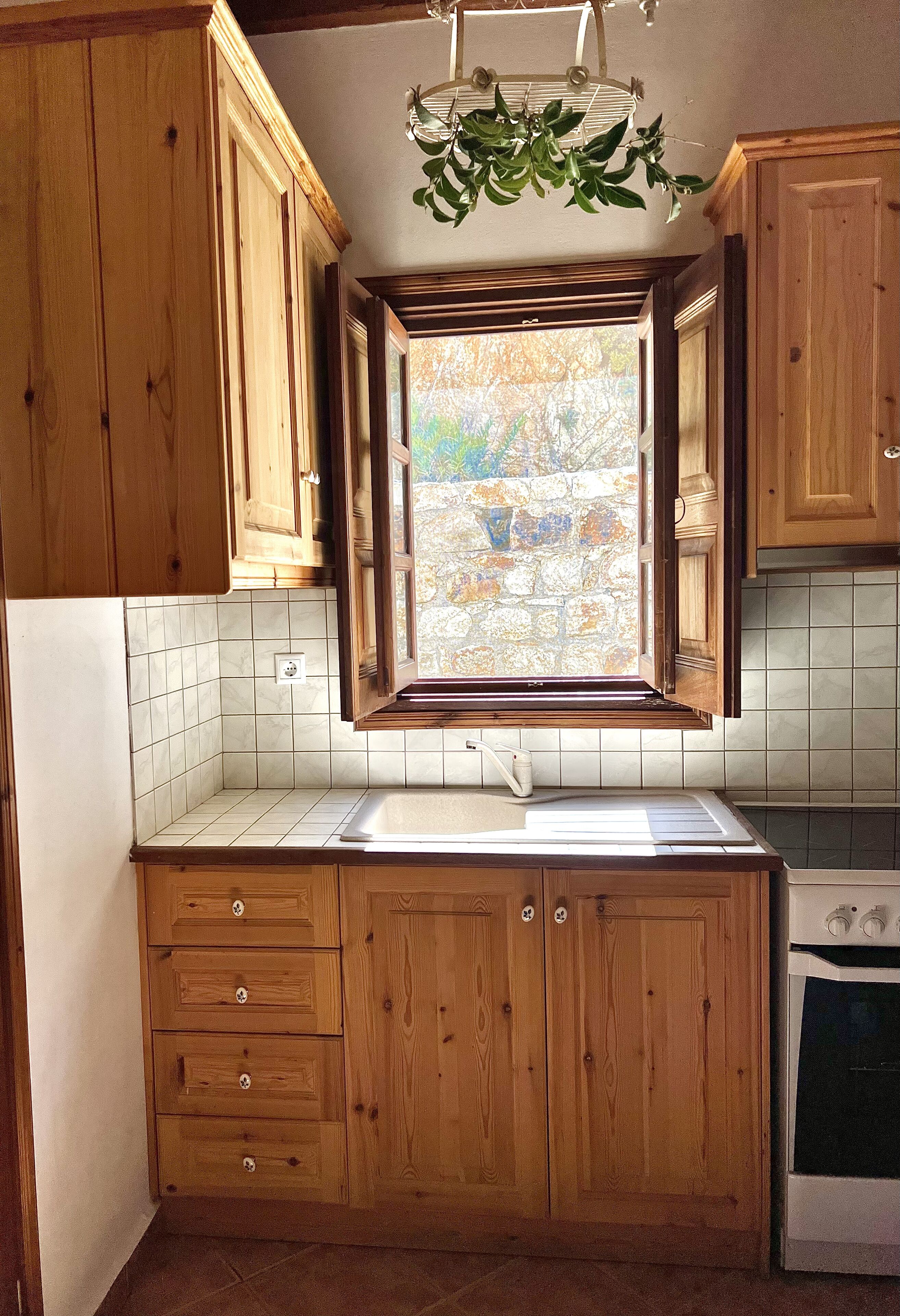 Una cocina con armarios de madera, una ventana con vista a un muro de piedra, un lavamanos y un horno.