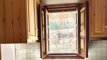 Una cocina con armarios de madera, una ventana con vista a un muro de piedra, un lavamanos y un horno.