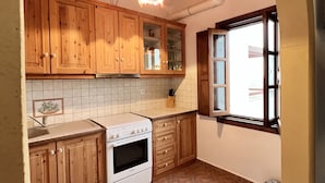 A kitchen with wooden cabinets, a stove, and a window. - Litois Houses Patmos (Patmos)