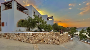 A modern building with a stone wall and a paved road leading to a view of the sea. - Litois Houses Patmos (Patmos)