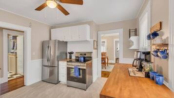A modern kitchen with stainless steel appliances, a wooden dining table, and a ceiling fan.