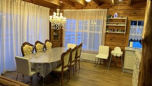 A wooden-paneled dining room with a marble table, upholstered chairs, a chandelier, and a view through large windows.
