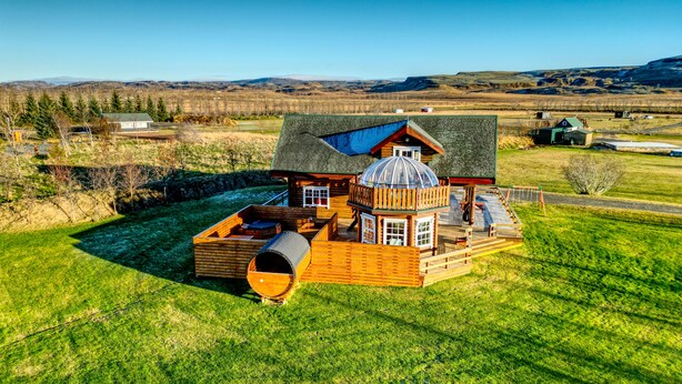 A wooden cabin with a large deck, a covered outdoor area, and a view of the surrounding landscape.