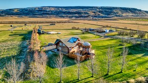 A large log cabin with a prominent tower, surrounded by expansive fields and a distant mountain range.