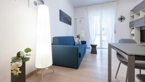 A modern living room with a blue sofa, a white lamp, and a dining table. - Italianway Comfort - Brenta 9 (Milan)
