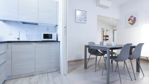 A modern kitchen with white cabinets, a microwave, and a dining area with a table and chairs. - Italianway Comfort - Brenta 9 (Milan)