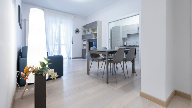 A modern kitchen with white cabinets, a dining table with four chairs, and a large window with sheer curtains. - Italianway Comfort - Brenta 9 (Milan)