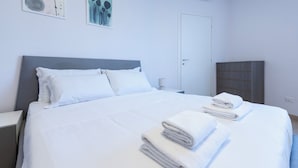 A neatly made bed with white linens and pillows, a bedside table with a lamp, a wooden wardrobe, and two abstract paintings on the wall. - Italianway Comfort - Brenta 9 (Milan)