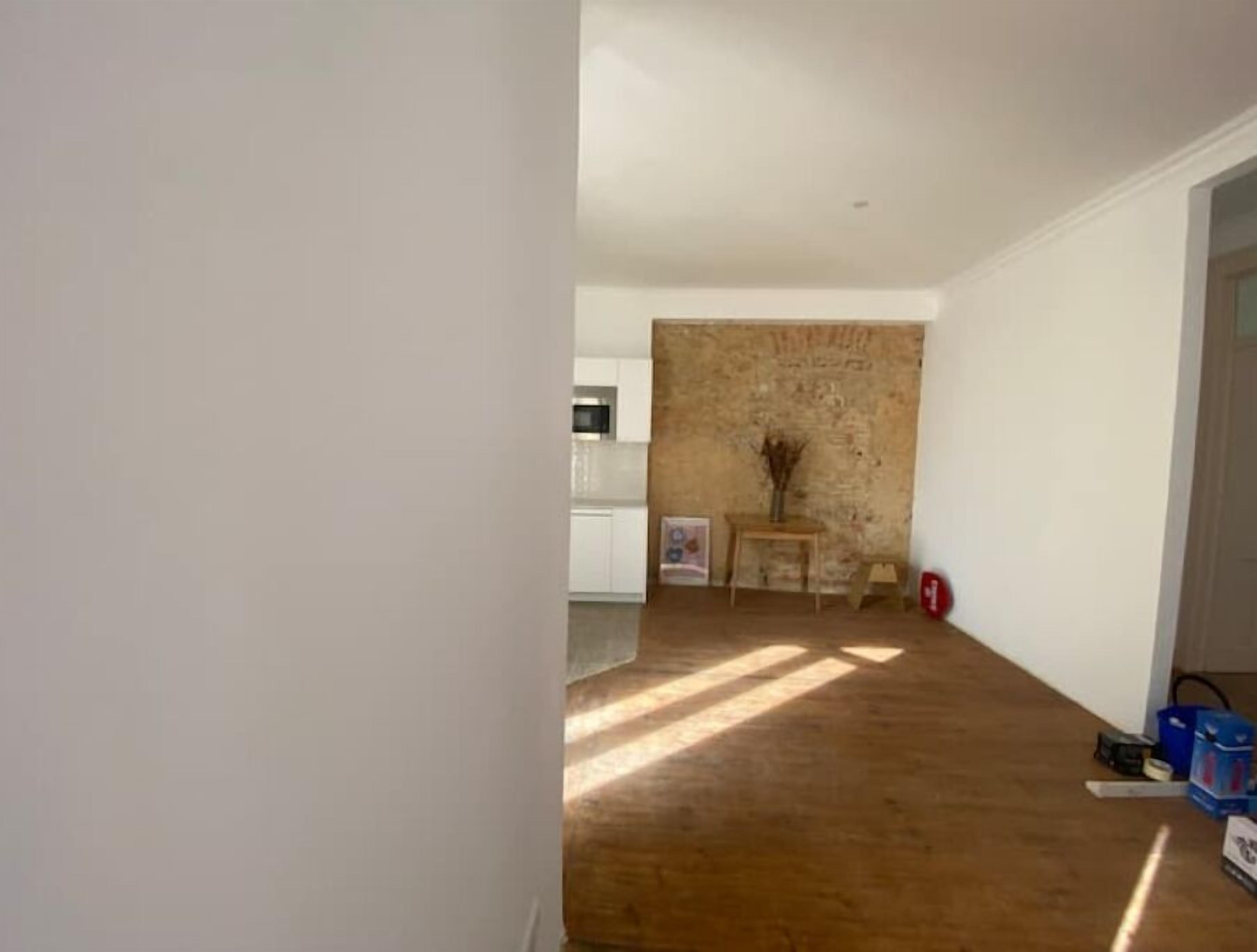 A room with a wooden floor, a brick wall, and a small table with a vase.