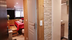 A compact room with a wooden door, a stone accent wall, and a small kitchenette. - Apart. cosy (47m²) - big family room - 3 bedrooms - directly on the slopes (Les Belleville)