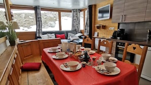 A cozy cabin interior with a dining table set for four, wooden benches, a sofa, and a kitchen area with a TV. - Apart. cosy (47m²) - big family room - 3 bedrooms - directly on the slopes (Les Belleville)