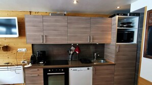 A modern kitchen with wooden cabinets, a built-in microwave, a dishwasher, and a stove. - Apart. cosy (47m²) - big family room - 3 bedrooms - directly on the slopes (Les Belleville)