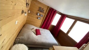 A compact room with a bed, a small table, and a window with curtains. - Apart. cosy (47m²) - big family room - 3 bedrooms - directly on the slopes (Les Belleville)