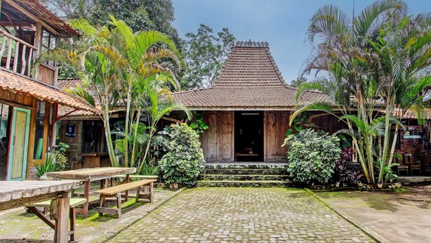 A traditional house with a tiled roof, surrounded by lush greenery and a cobblestone courtyard. - Hotel O Omah Baturan Syariah (Colomadu)