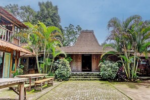 A traditional house with a tiled roof, surrounded by lush greenery and a cobblestone courtyard. - Hotel O Omah Baturan Syariah (Colomadu)