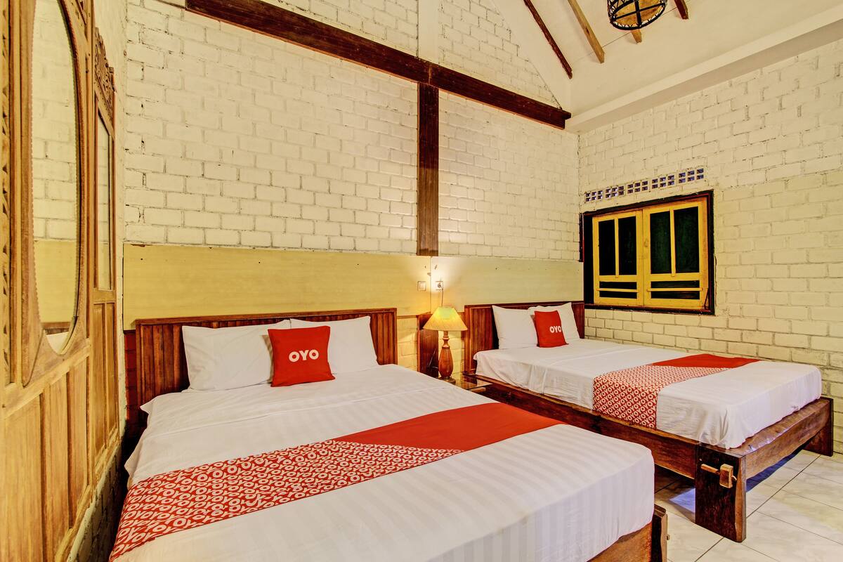 A hotel room with two beds, each with a wooden headboard, white bedding, and red accents.