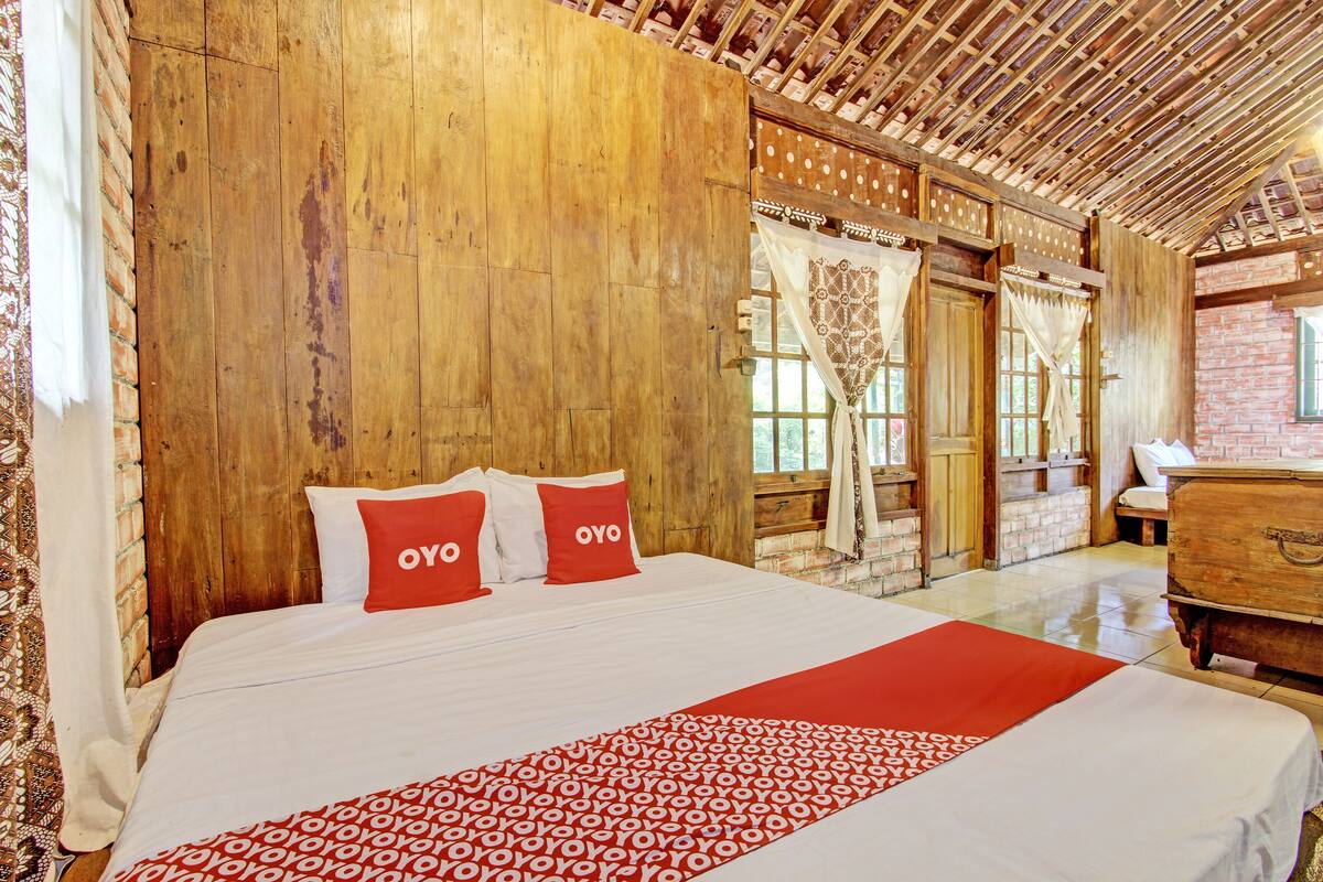 A wooden room with a bed, a wooden dresser, and a window with curtains.