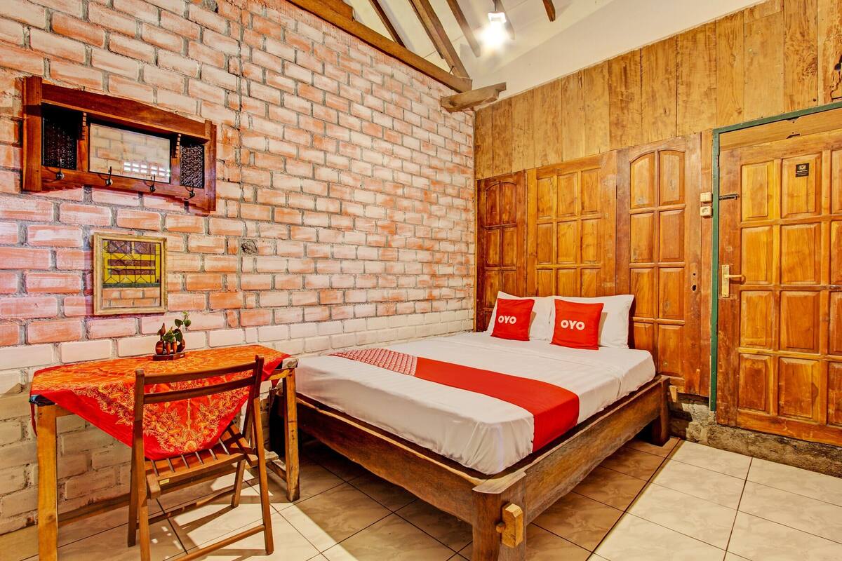 A room with a brick wall, wooden door, and a bed with red and white bedding.