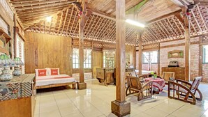 A rustic room with a wooden bed, a dining table with chairs, and a wooden desk. - Hotel O Omah Baturan Syariah (Colomadu)