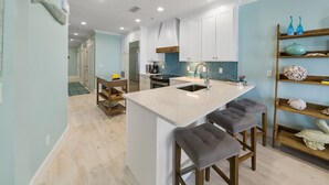 Une cuisine moderne avec des meubles blancs, un îlot central doté de tabourets de bar et un pare-feu bleu.