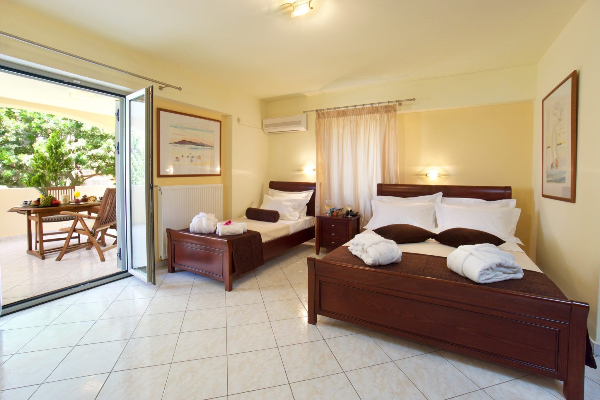 Quarto de hotel com duas camas, área de refeições com mesa e cadeiras, e vista através de uma porta de vidro.
