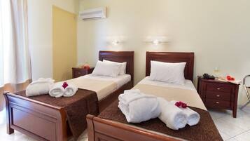 A hotel room with two beds, each with a brown headboard, white linens, and towels. There is a nightstand with a lamp and a phone, and an air conditioning unit on the wall.