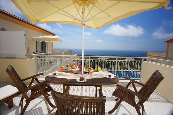 Balcón con mesa lista para el desayuno, con vista a una piscina y al océano.
