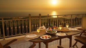 Mesa lista para dos con platos, vasos y una cesta de pan en un balcón con vistas panorámicas.