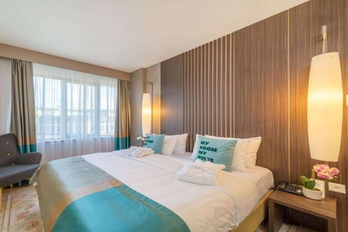A hotel room with a large bed, a sofa, a desk, and a window with curtains.
