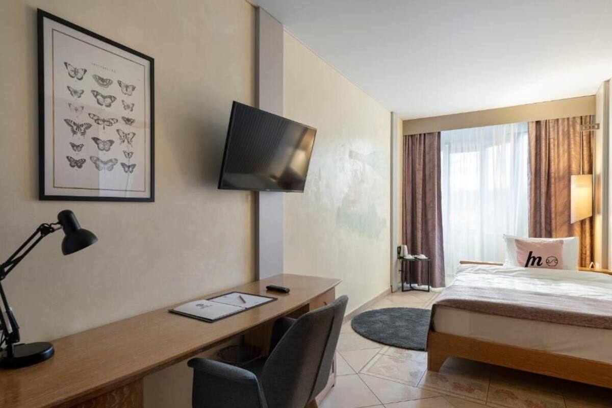 A hotel room with a desk, chair, bed, TV, and a framed butterfly artwork.