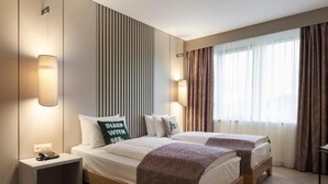 Une chambre d’hôtel avec deux lits, une table de chevet avec un téléphone et une fenêtre avec des rideaux.