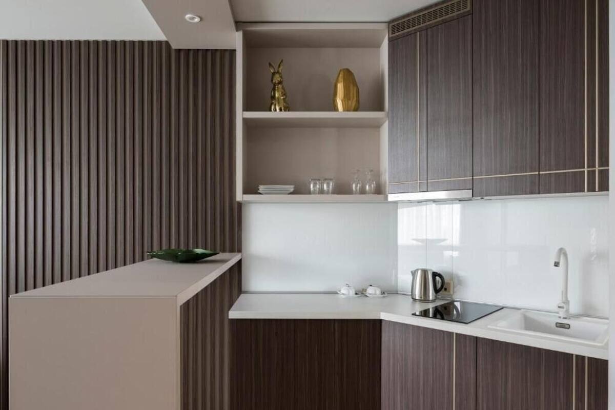 A modern kitchen with dark wood cabinets, a white countertop, and a built-in shelf with decorative items.