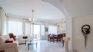 Uma sala de estar ampla, com sofá, mesa de centro e área de jantar com cadeiras.