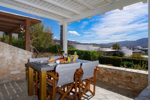 A terrace with a table set for breakfast, overlooking a scenic landscape with buildings and hills. - Olivia's Countryside House (Paros)