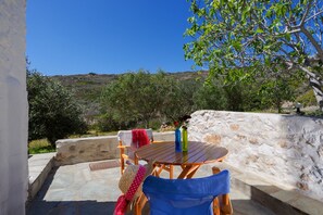 An outdoor seating area with a table and chairs, a stone wall, and a view of a hilly landscape. - Olivia's Countryside House (Paros)