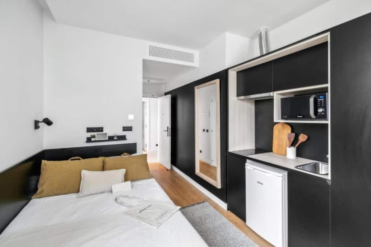 Ein modernes Schlafzimmer mit einem Bett, Nachttischen und einer kleinen Küchenzeile mit Mikrowelle und Spüle.