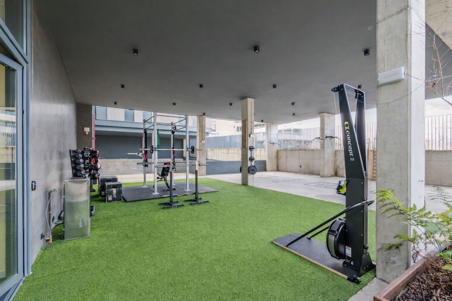 Un gimnasio al aire libre con equipo de ejercicio, césped artificial y pilares de concreto.
