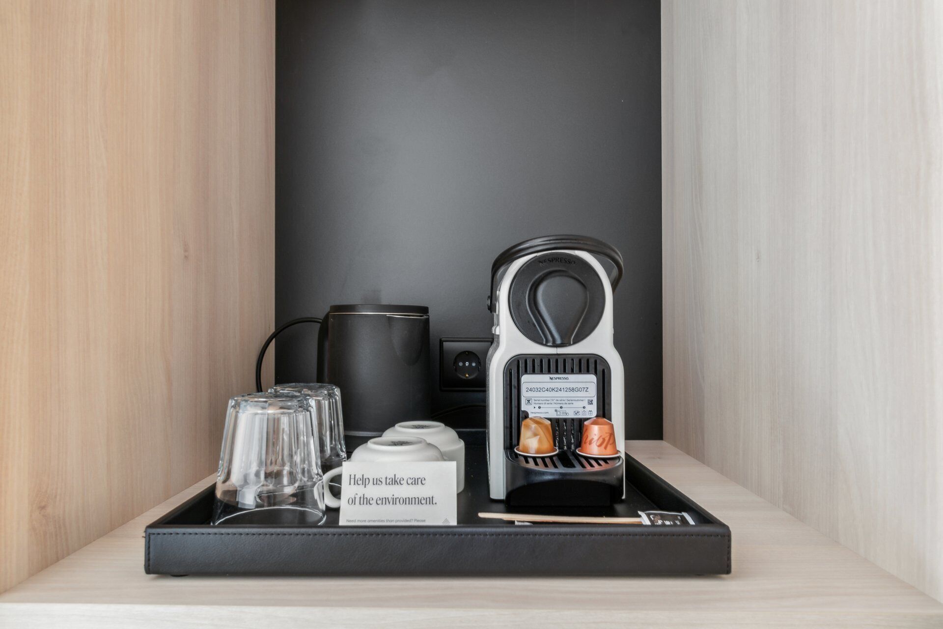 Eine Kaffeemaschine, ein Wasserkocher und eine Ablage mit Gläsern sowie ein Schild auf einem Holzregal.