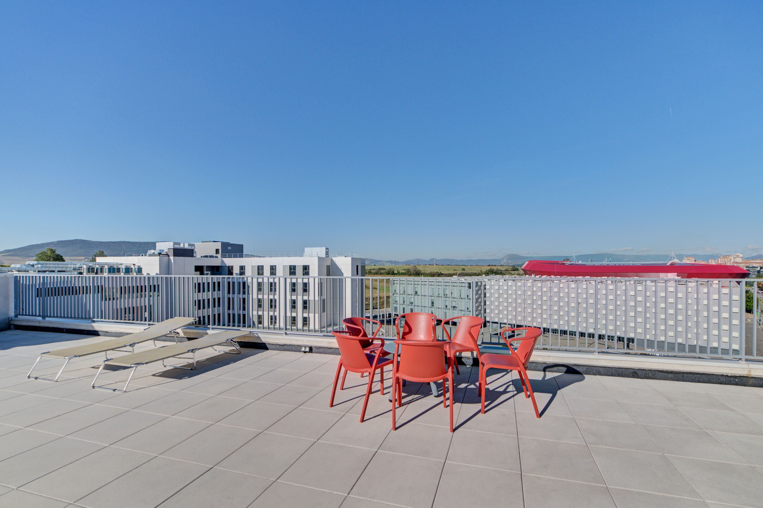 A rooftop terrace with a table and chairs, a pool, and a view of a cityscape and mountains.