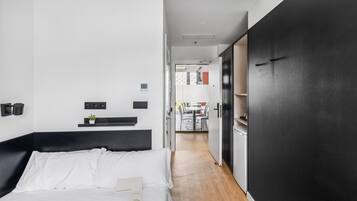 Une chambre d’hôtel moderne, équipée d’un lit, d’une table de chevet, d’une petite plante et offrant une vue sur la cuisine.