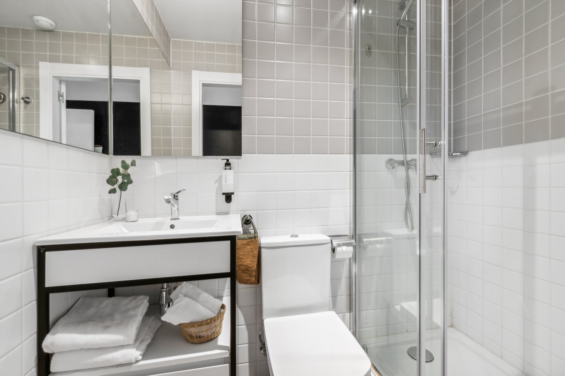 A modern bathroom with a white sink, mirror, and glass shower enclosure.