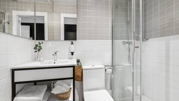 A modern bathroom with a white sink, mirror, and glass shower enclosure.